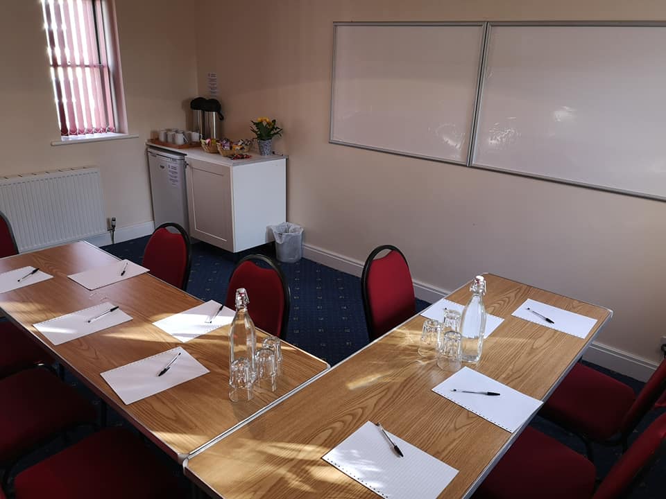 image of St Augustine's room with two long tables set out, surrounded by chairs, and two white boards on the wall. In the corner is a cupboard with coffee and tea making facilities