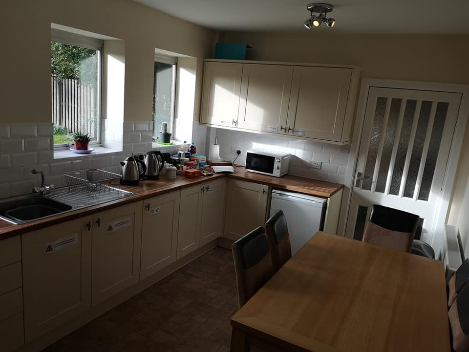 image of fully fitted kitchen with cupboards, appliances, kettles and a microwave. There is a also a large table with six chairs